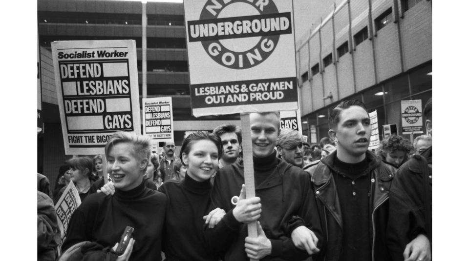 Image of A black and white photograph of people marching holding placards. One reads 'Never Going Underground - Lesbians & Gay Men Out and Proud'