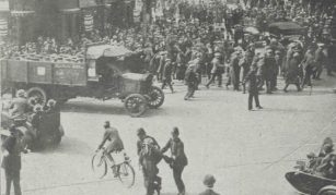 Image of Historic black-and-white photograph of a crowded street in Hammersmith Broadway, with police arresting a man during the passage of a milk lorry, surrounded by onlookers, vehicles, and a mounted policeman in the background.