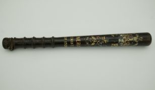 Image of Photograph of a vintage black wooden truncheon with a textured grip and faded gold lettering along its length. The text includes May 1926.