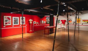 Image of A red wall hung with framed pictures and mounted t-shorts in an exhibition