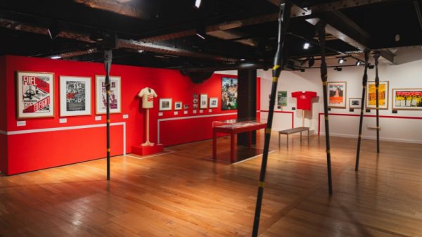 Image of A red wall hung with framed pictures and mounted t-shorts in an exhibition