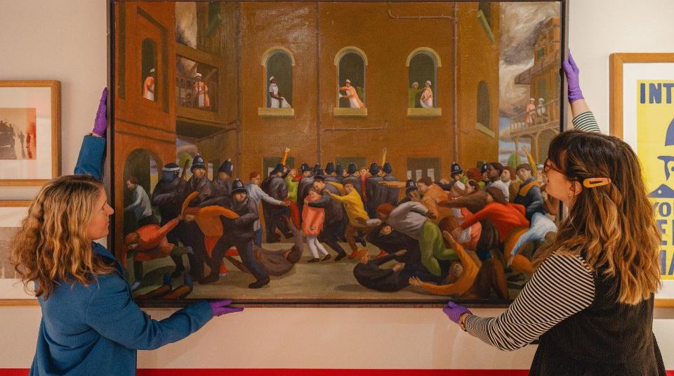 Image of Two people installing a large painting on a gallery wall