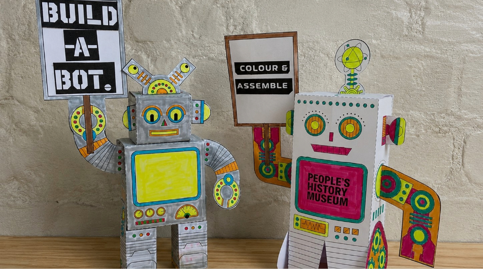 Image of Colour photograph of two mini robot models made from sheets of paper.