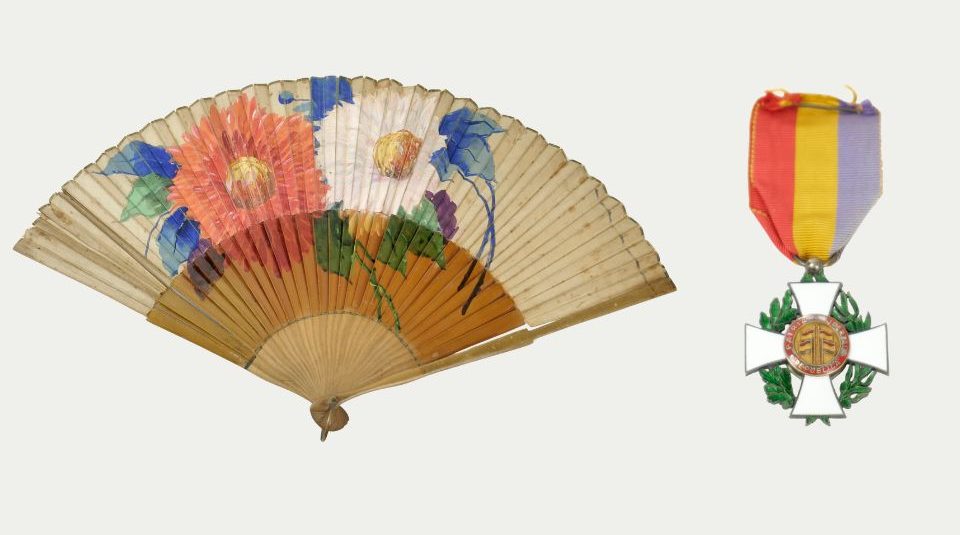 Image of Left to right: colour photograph of a traditional hand fan featuring a painted floral design with large red, white, and purple flowers and green leaves, and a photograph of a medal featuring a white cross with green laurel leaves behind, attached to a vertically striped ribbon in red, yellow, and purple.