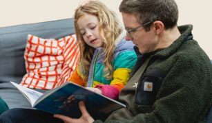 Image of Child and adult sat down reading a book together.