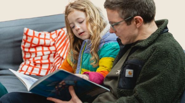 Image of Colour photograph of a child and adult sat down reading a book together.