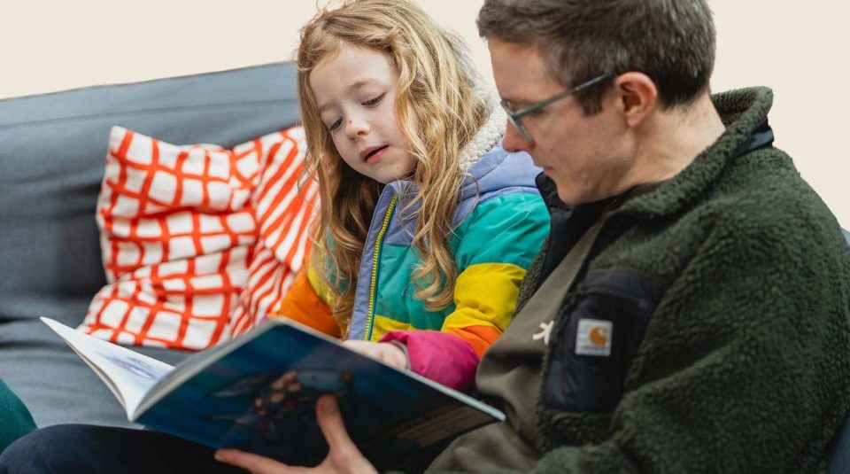 Image of Child and adult sat down reading a book together.
