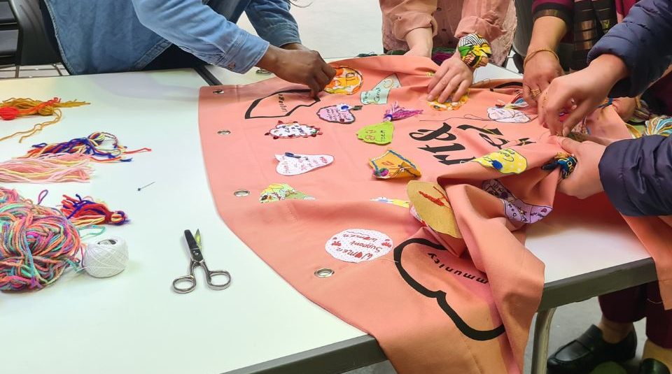 Image of Four pairs of hands stitching a textile on a table top