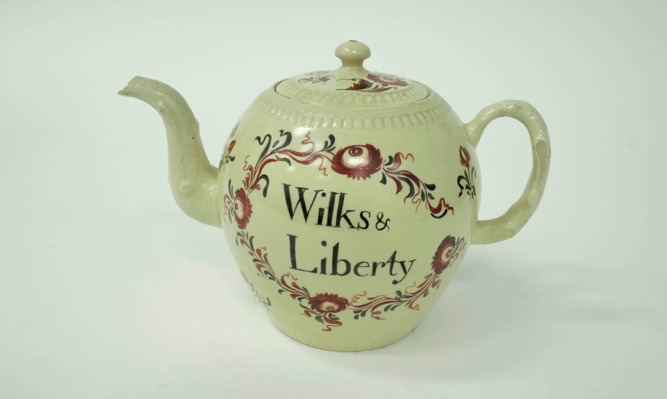 Colour photograph of a ceramic teapot featuring floral designs in red and green with the words: 'Wilks & Liberty' prominently displayed on its body.