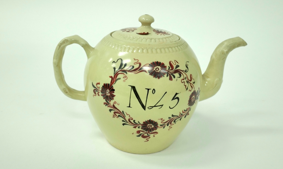 Colour photograph of a ceramic teapot featuring floral designs in red and green with the words ‘No 45’ prominently displayed on its body.