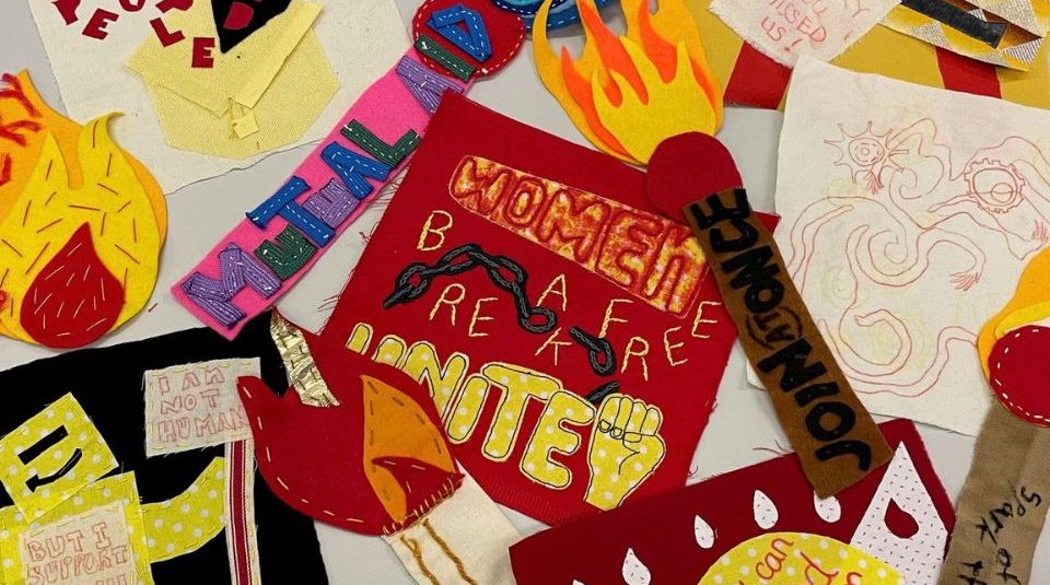 Image of A photograph of various handmade fabric patches featuring messages including a red patch with a raised fist and text 