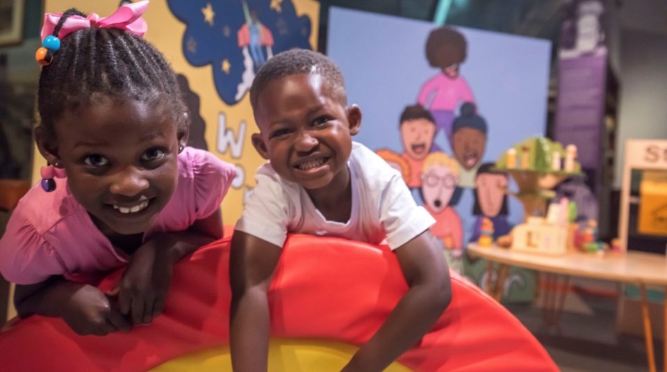 Image of Photograph of two children against a background of vibrant cartoon murals