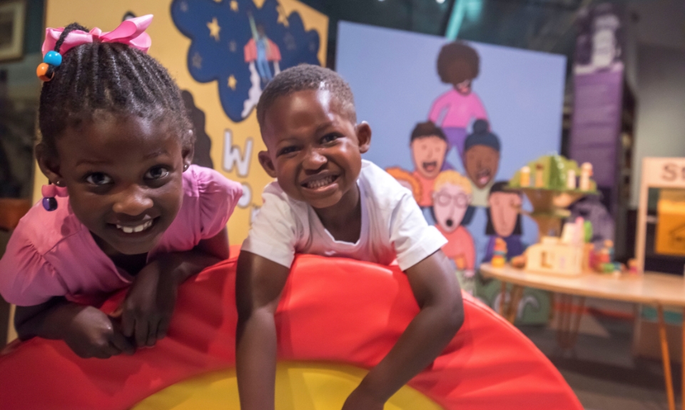 Colour photograph of two smiling children against a background of vibrant cartoon murals.