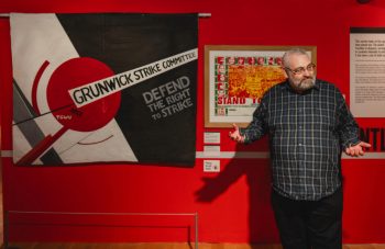 Image of A black and white banner with a geometric design including a large red circle, and text including: 'Grunwick Strike Committee, Defend The Right To Strike'.