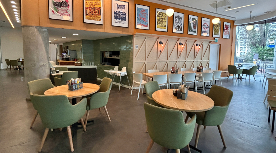 Colour photo of a café, with chairs and tables and vibrant artwork along the wall.