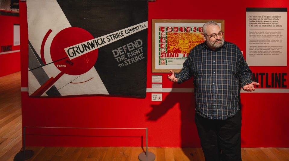 Image of A black and white banner with a geometric design including a large red circle, and text including: 'Grunwick Strike Committee, Defend The Right To Strike'.