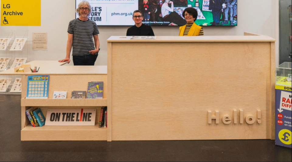 Three people stood behind a museum welcome desk.