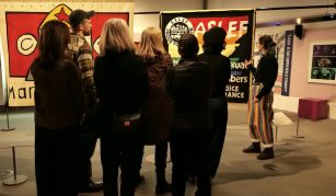 Image of Colour photograph of a group of people on a guided gallery tour, including large colourful textile banners on display.