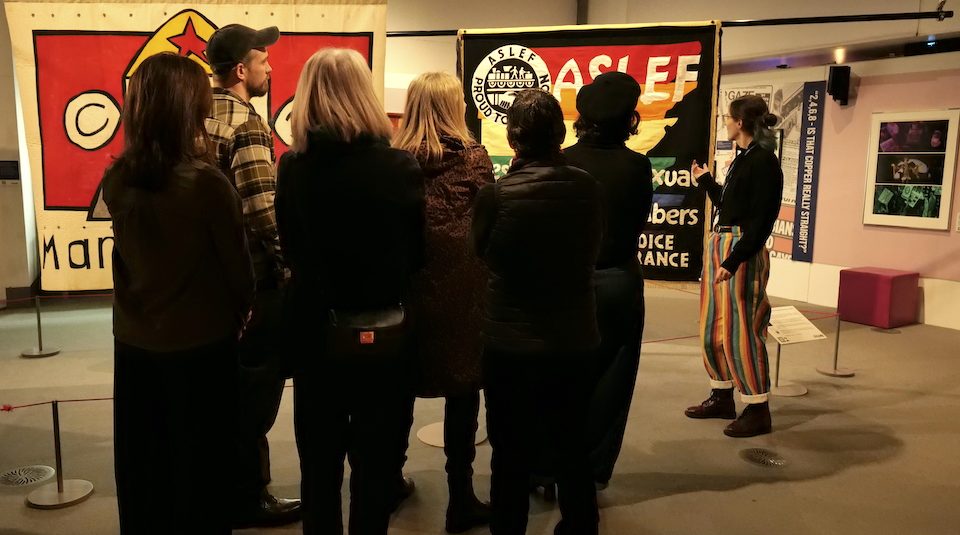 Image of Colour photograph of a group of people on a guided gallery tour, including large colourful textile banners on display.