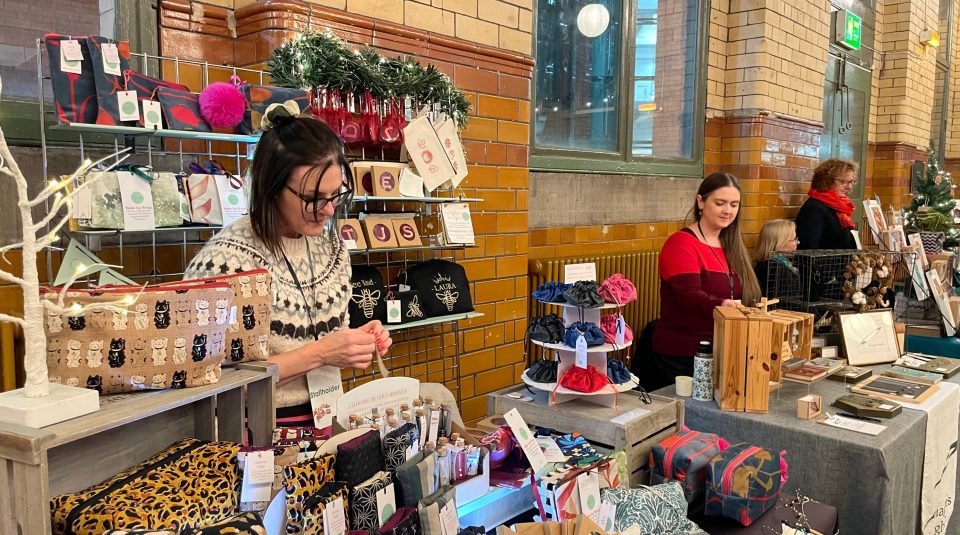Image of A number of stallholders standing in a row in front of their display of gifts they are selling at the market.